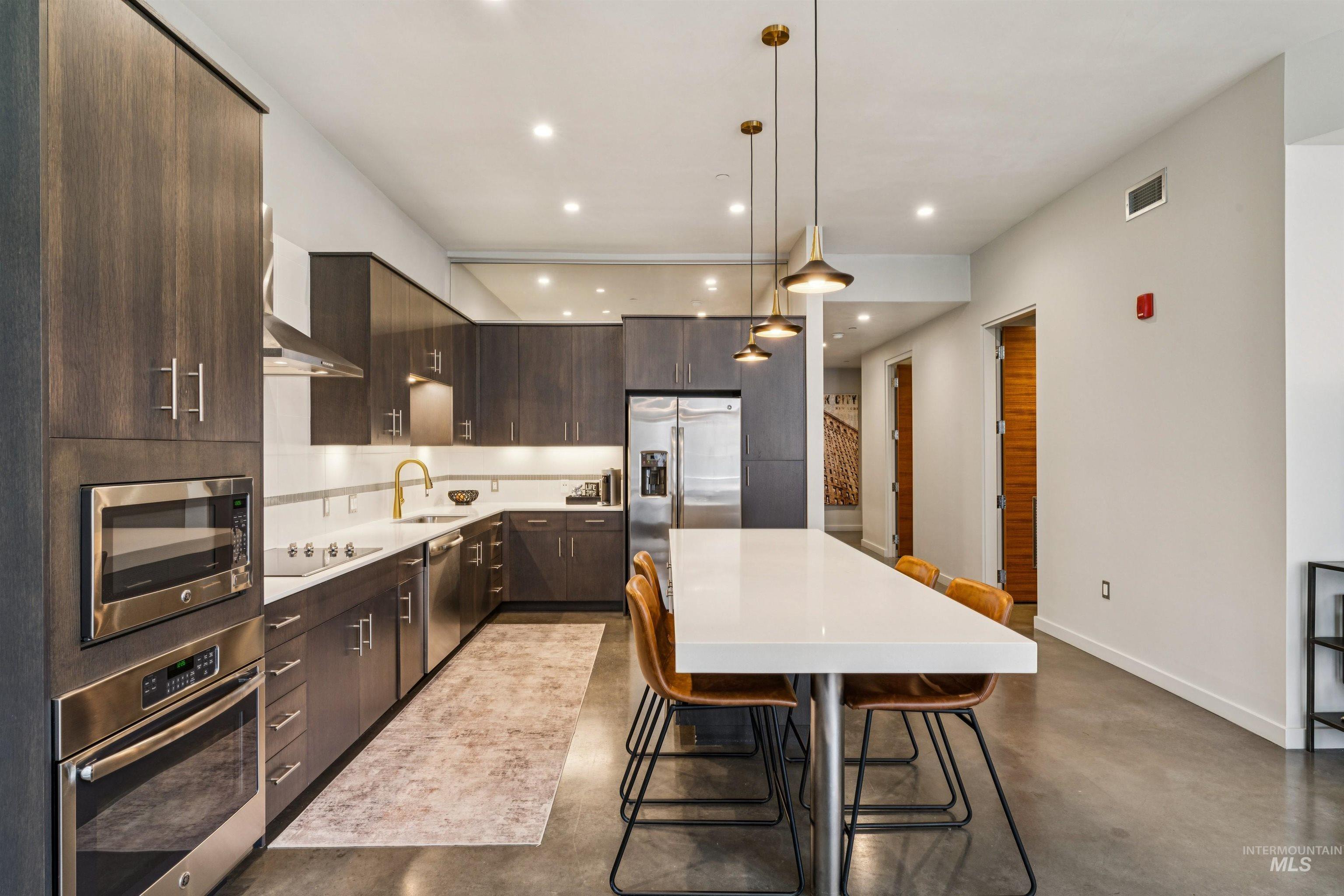119 South 10th Street, Unit 307 Boise, ID 83702 - Photo 18 of 47 Modern kitchen featuring dark wood-finish cabinetry, stainless steel appliances, a white subway tile backsplash, and a large central island with pendant lighting