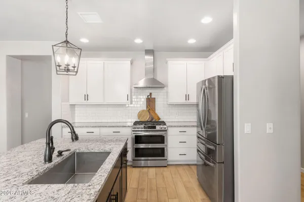 a kitchen with stainless steel appliances granite countertop a refrigerator a sink dishwasher a stove and a dining table with wooden floor