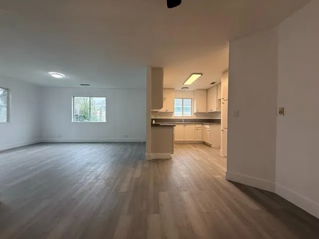 a view of a kitchen and an empty room with wooden floor and a window