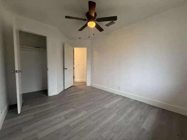 an empty room with wooden floor chandelier fan and windows