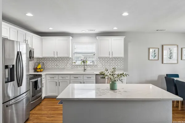 a kitchen with stainless steel appliances granite countertop a sink a stove a refrigerator cabinets a dining table and chairs