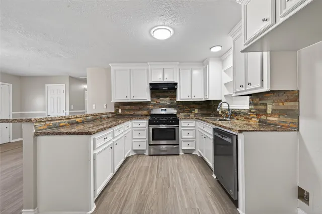 a kitchen with stainless steel appliances granite countertop a stove top oven a sink dishwasher and a refrigerator with wooden floor