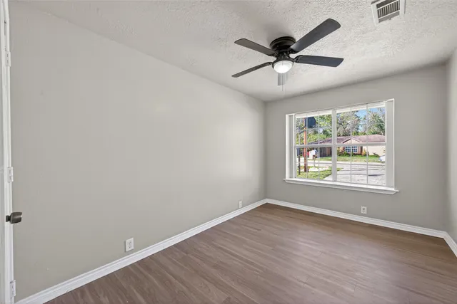 an empty room with wooden floor ceiling fan and window