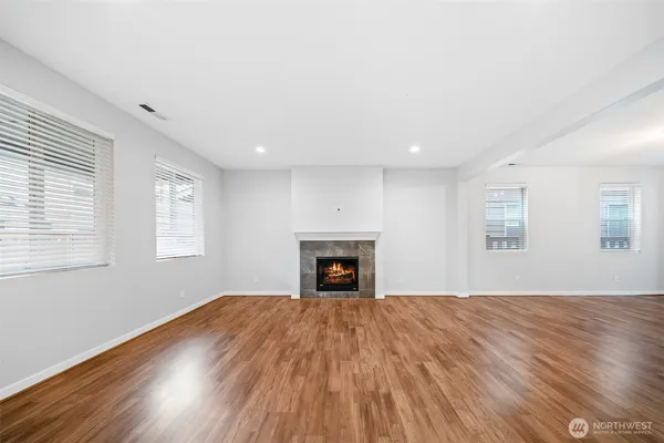 a view of an empty room with wooden floor fireplace and a window