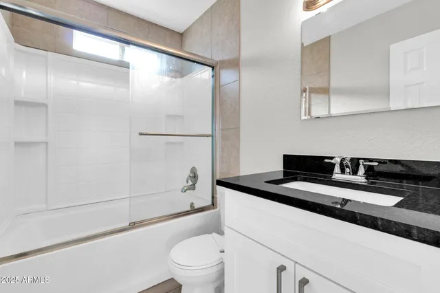 a bathroom with a granite countertop sink a toilet a mirror and shower