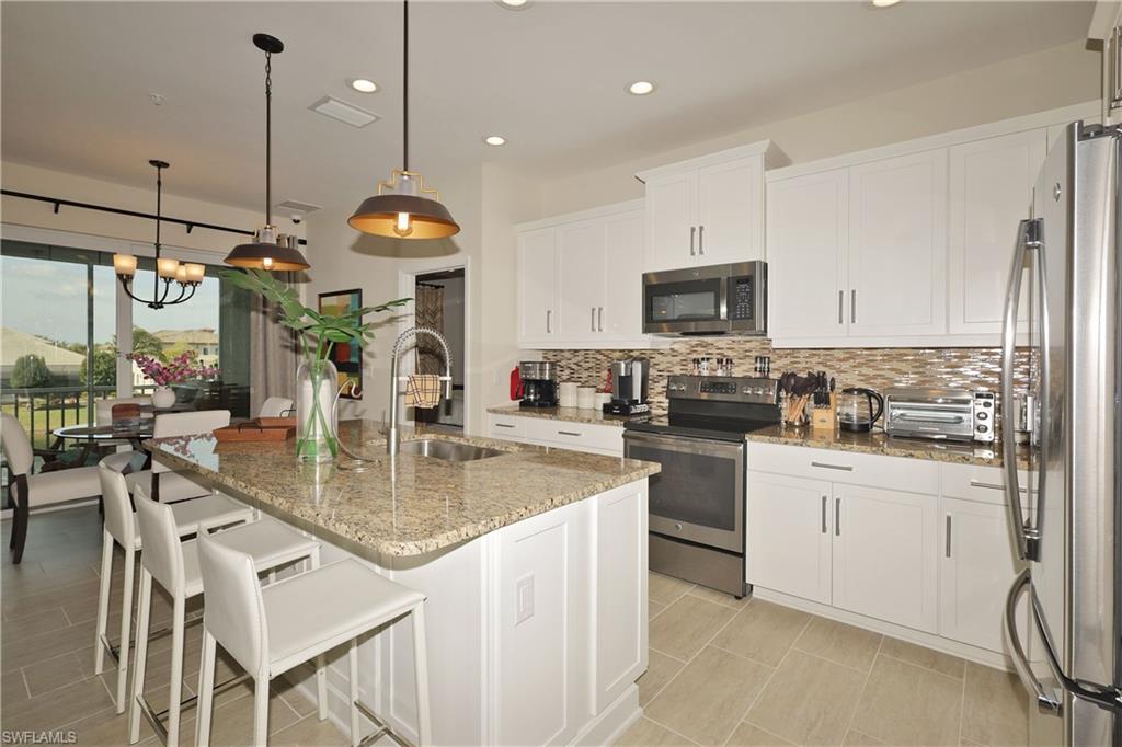 a kitchen with stainless steel appliances granite countertop a stove top oven a refrigerator a sink and white cabinets