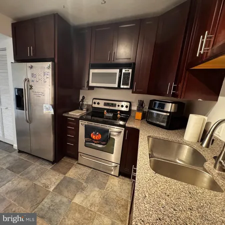 a kitchen with stainless steel appliances granite countertop a refrigerator a stove and a sink with wooden cabinets