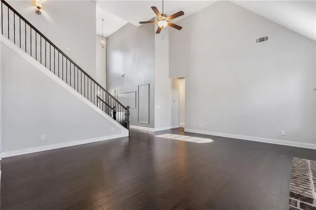 a view of an empty room with wooden floor and a ceiling fan