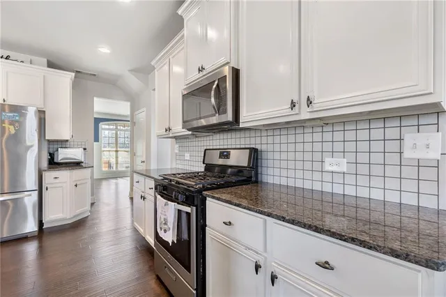 a kitchen with stainless steel appliances granite countertop a stove a sink and white cabinets