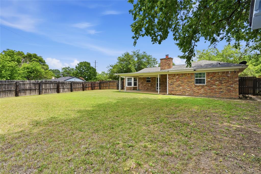 837 Springdale Road Bedford, TX 76021 - Photo 25 of 28 Expansive grassy backyard featuring a full privacy fence, brick exterior with multiple windows, covered patio, and a brick chimney