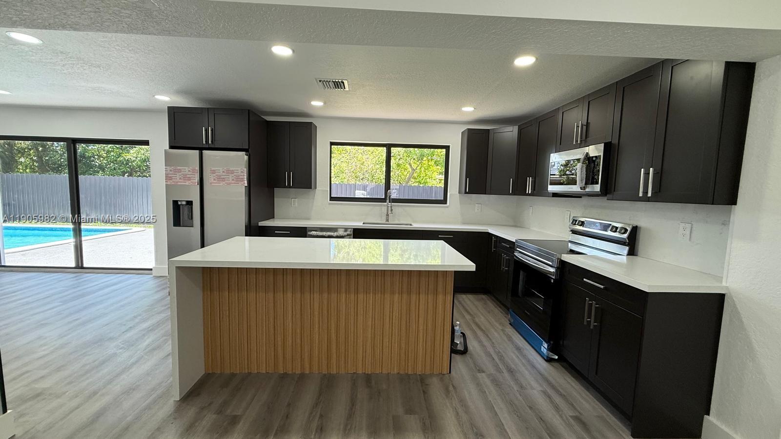 20 Northwest 197th Street Miami Gardens, FL 33169 - Photo 22 of 48 a kitchen with kitchen island granite countertop a sink appliances wooden floor and a large window