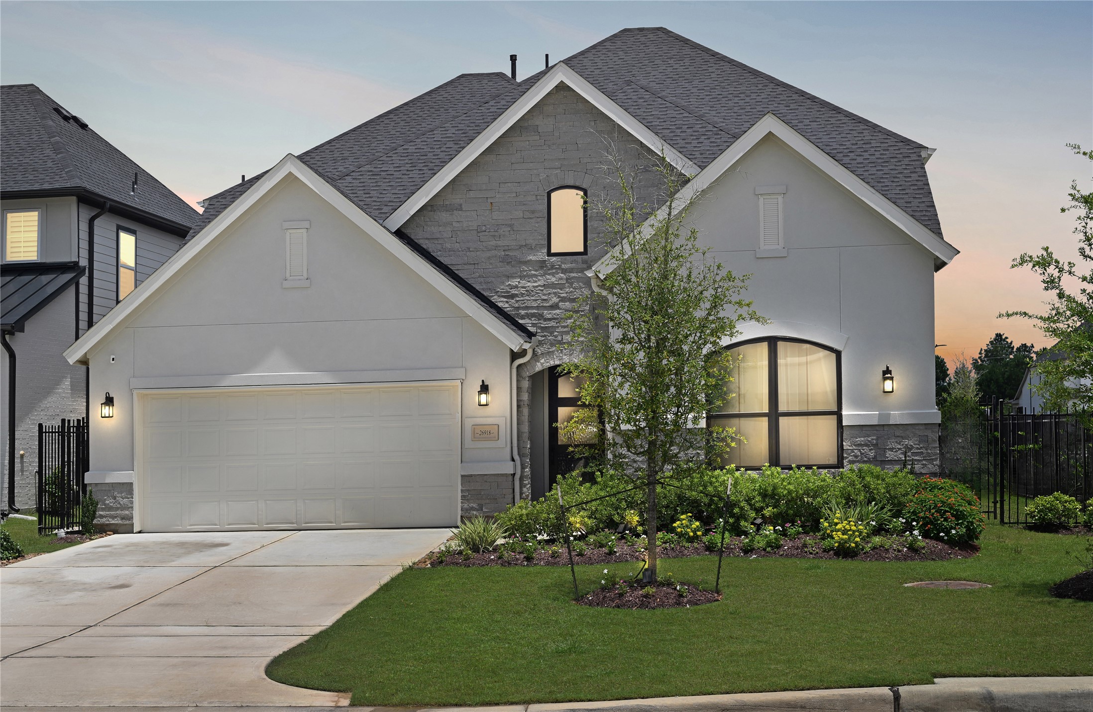 Welcome to 26918 Swanborough Rd. This beautiful corner lot showcases a spacious, elegant two-story home with a striking stone and stucco exterior, warmly lit at dusk.