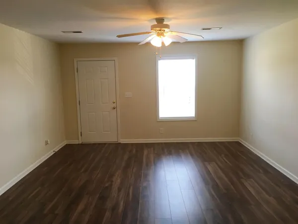 a view of an empty room with wooden floor and a window