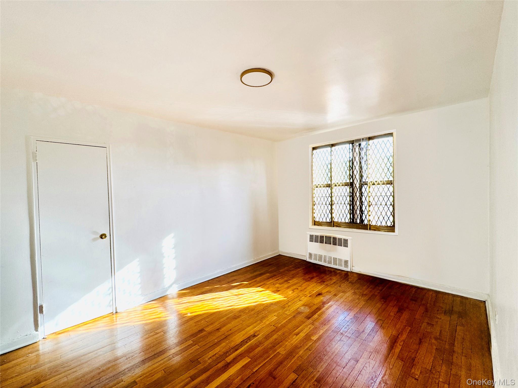 141-05 Pershing Crescent, Unit 207 Queens, NY 11435 - Photo 11 of 13 an empty room with wooden floor and windows