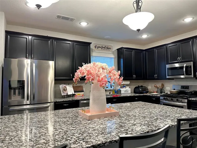 a kitchen with kitchen island granite countertop stainless steel appliances a sink refrigerator stove microwave and cabinets