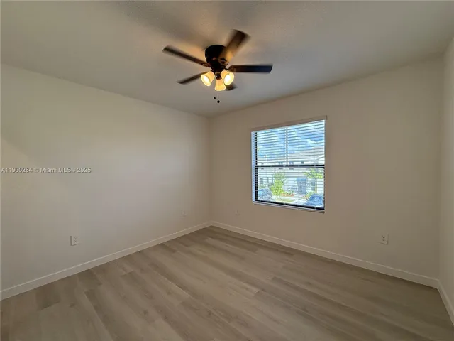 an empty room with wooden floor ceiling fan and windows