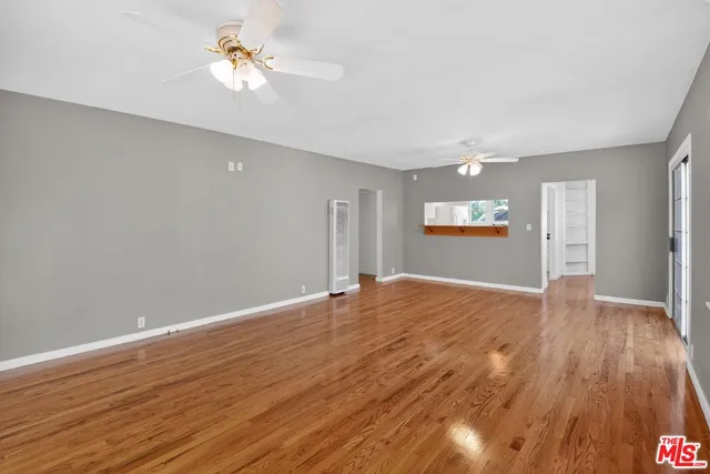 a view of empty room with wooden floor and fan