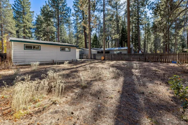 a backyard of a house with large trees and wooden fence