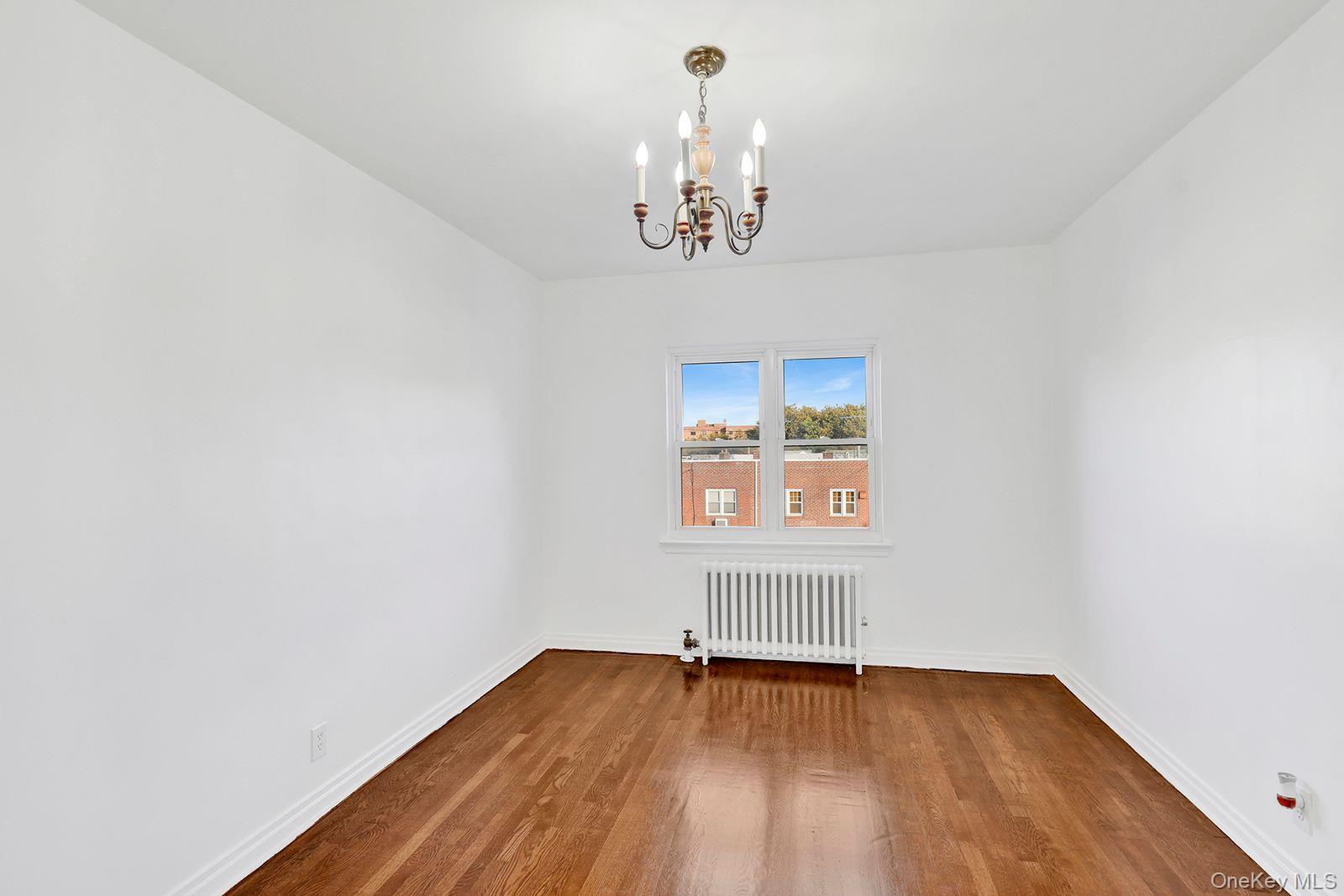102-12 62nd Road Queens, NY 11375 - Photo 15 of 27 an empty room with wooden floor chandelier and windows