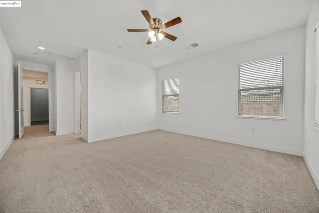an empty room with chandelier fan and windows
