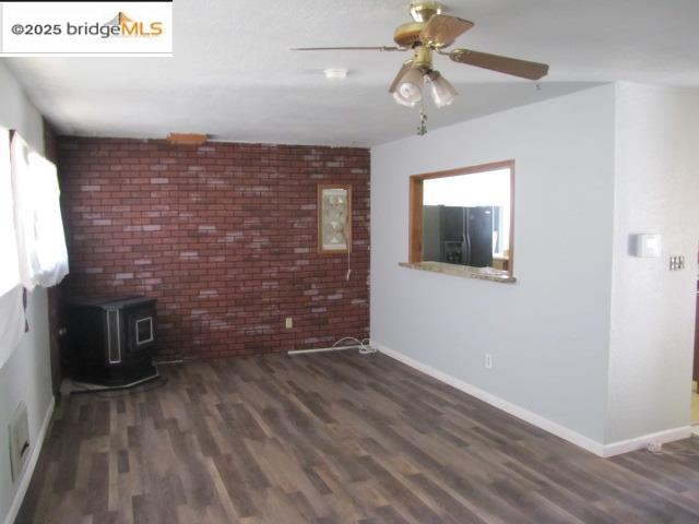 1943 South Ranchero Road Valley Springs, CA 95252 - Photo 13 of 23 Unfurnished living room featuring a wood stove, brick wall, dark wood-style flooring, and ceiling fan