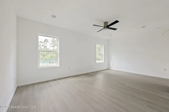 an empty room with wooden floor ceiling fan and windows