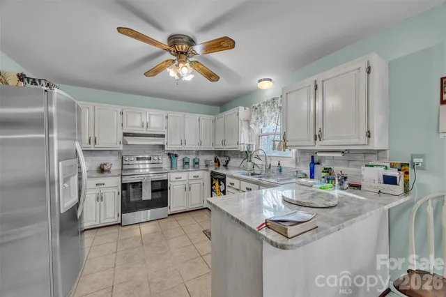 a kitchen with stainless steel appliances granite countertop a sink a stove a refrigerator cabinets and chairs