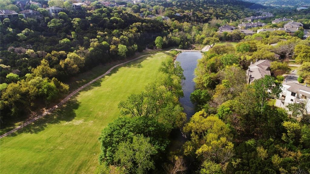 9201 Simmons Road, Unit 117 Austin, TX 78759 - Photo 3 of 11 Expansive green space featuring a winding path, bordered by mature trees and a tranquil water body