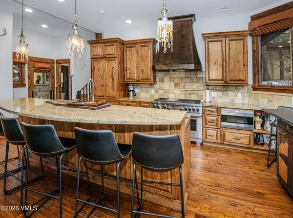 a kitchen with stainless steel appliances granite countertop a stove top oven a sink a dining table and chairs with wooden floor