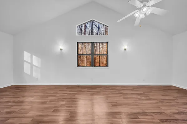 an empty room with wooden floor chandelier fan and windows