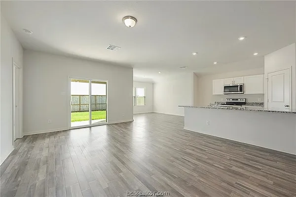 a view of an empty room with wooden floor and a kitchen