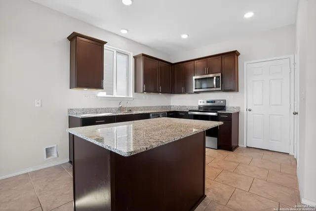 a kitchen with kitchen island granite countertop a stove top oven a sink a counter top space and cabinets
