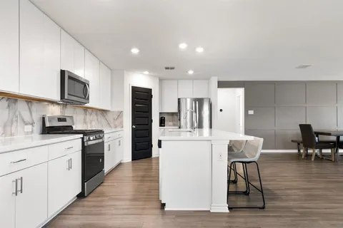 a kitchen with stainless steel appliances kitchen island granite countertop a refrigerator a stove top oven a sink a dining table and chairs with wooden floor