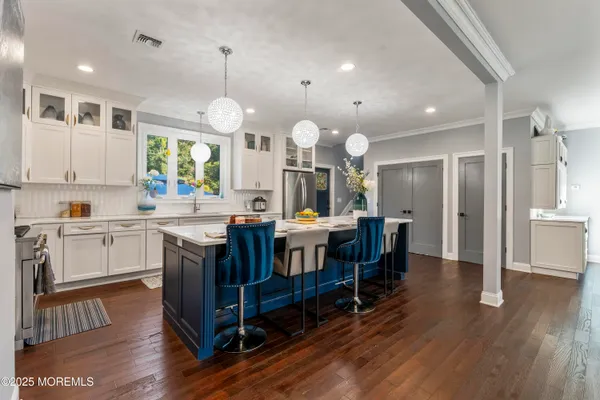 a kitchen with stainless steel appliances granite countertop a refrigerator a sink dishwasher a stove and white cabinets with wooden floor