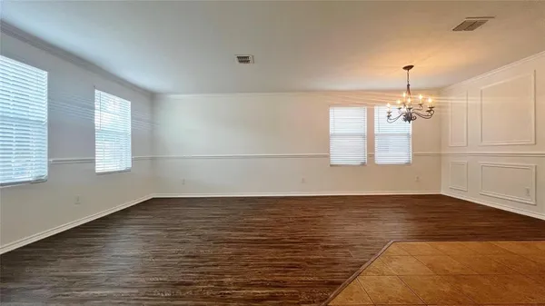 an empty room with wooden floor chandelier and windows