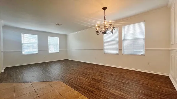 an empty room with wooden floor chandelier and windows