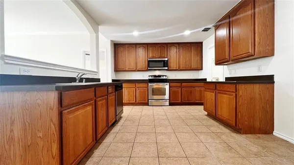 a large kitchen with stainless steel appliances granite countertop a stove top oven a sink dishwasher and wooden cabinets