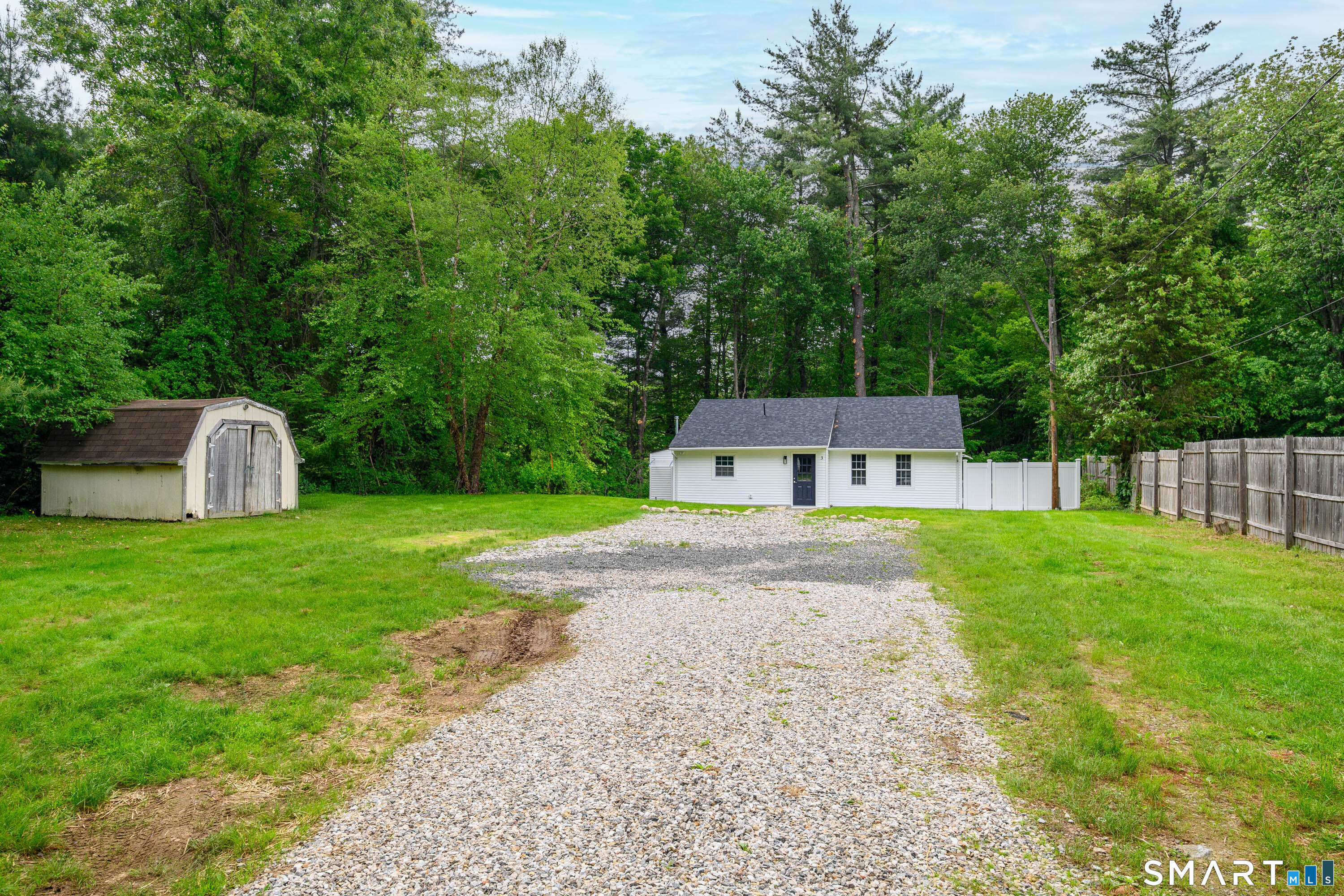 Spacious gravel driveway with ample parking and private wooded surroundings.