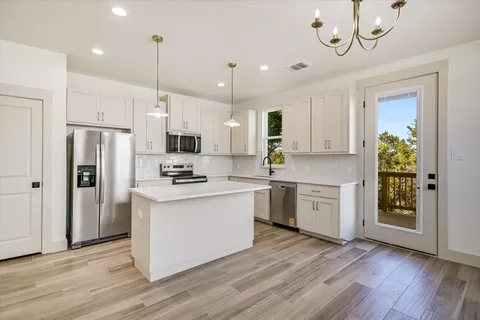 a kitchen with stainless steel appliances granite countertop a refrigerator a sink dishwasher a stove and white cabinets with wooden floor