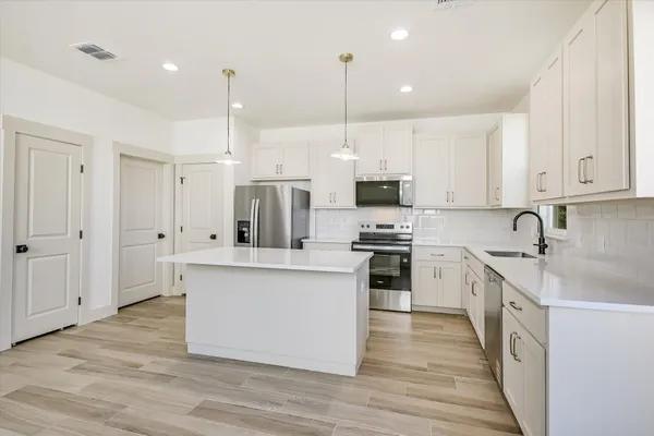 a large kitchen with stainless steel appliances sink a stove and white cabinets with wooden floor