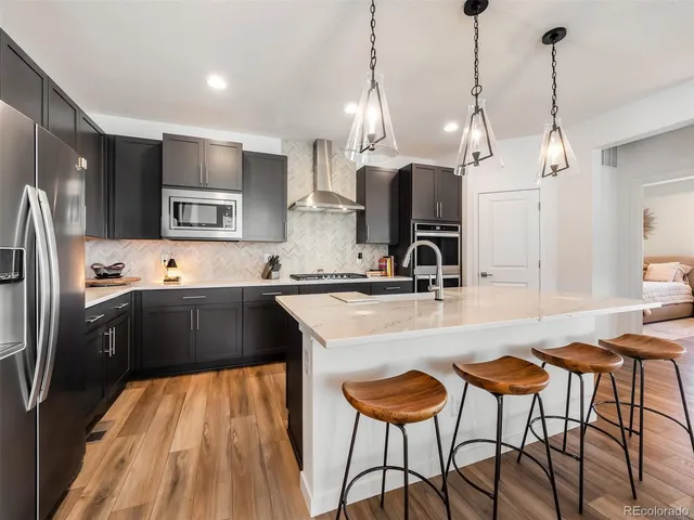 a kitchen with stainless steel appliances kitchen island granite countertop a sink a stove a refrigerator and island with wooden floor