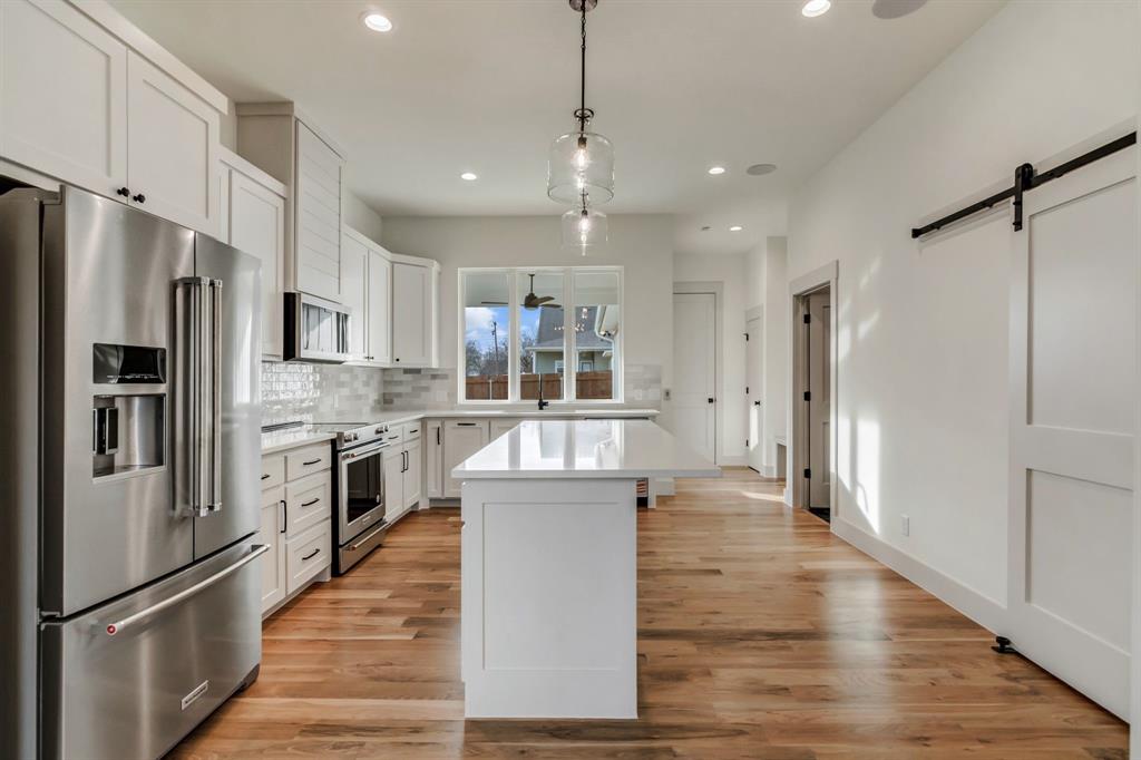 205 West 7th Street Justin, TX 76247 - Photo 12 of 35 a kitchen with kitchen island a counter top space a refrigerator cabinets and a wooden floor