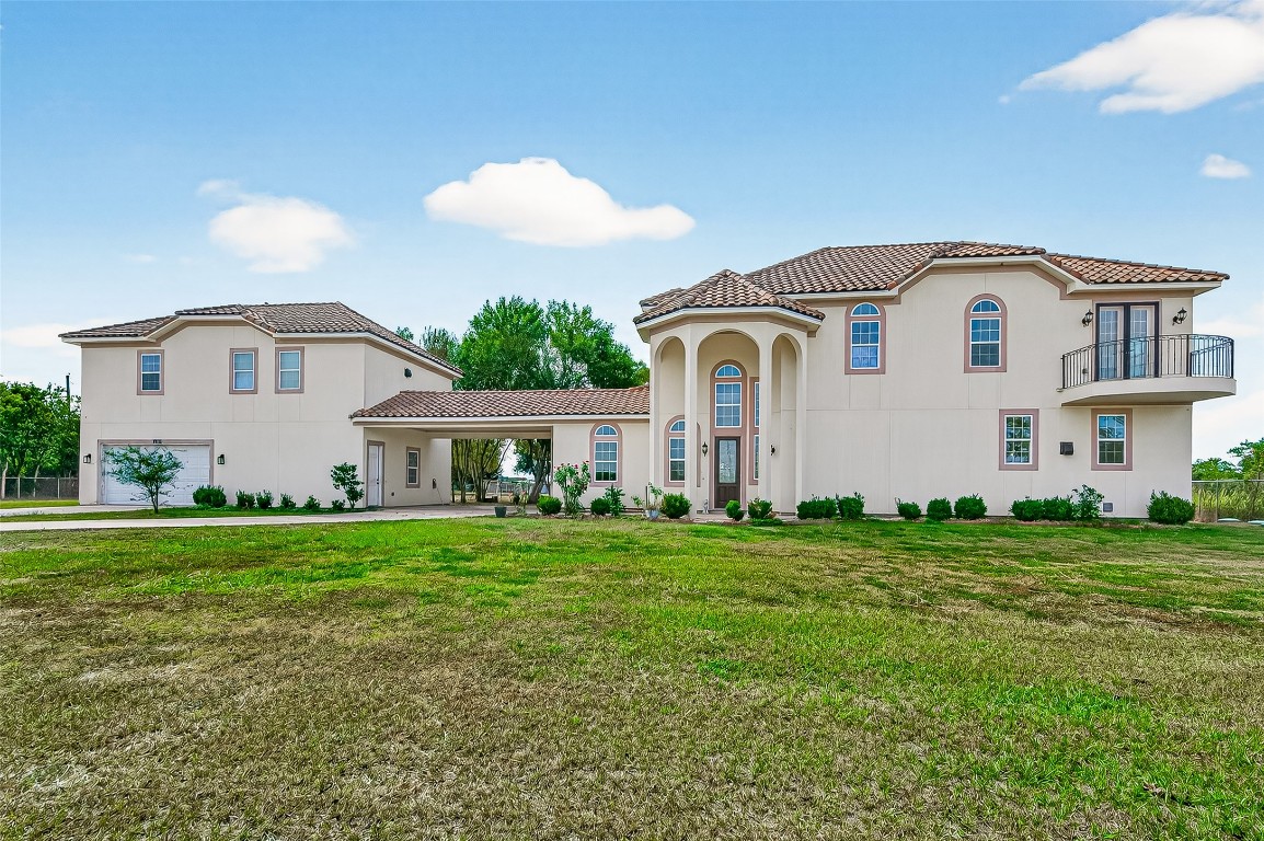 This photo showcases a spacious, elegant two-story Mediterranean-style home with a stucco exterior and terracotta roof tiles. It features arched windows, a small balcony, and a grand entrance with columns, set on a large, manicured lot.