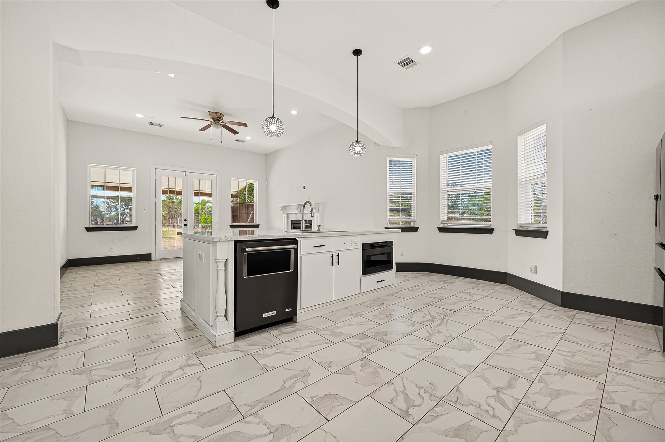 7915 Kirk Road Rosenberg, TX 77471 - Photo 12 of 28 This photo showcases a spacious, open-concept kitchen and living area with modern white cabinetry, a central island, and stylish hanging lights. The room is well-lit with large windows and a ceiling fan, and features elegant tile flooring.