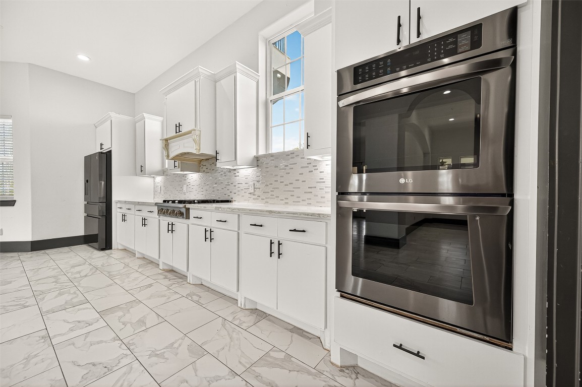 7915 Kirk Road Rosenberg, TX 77471 - Photo 13 of 28 This modern kitchen features sleek white cabinetry, stainless steel appliances, and a stylish tile backsplash. The spacious layout is enhanced by large windows that bring in plenty of natural light, creating an inviting and functional space.