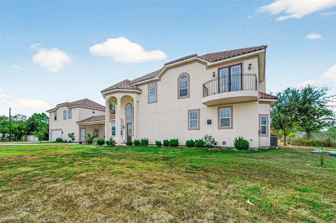 7915 Kirk Road Rosenberg, TX 77471 - Photo 2 of 28 This photo showcases a spacious two-story home with a Mediterranean style, featuring a stucco exterior and red-tiled roof. It includes a charming balcony and arched entryway, surrounded by a large, open yard.