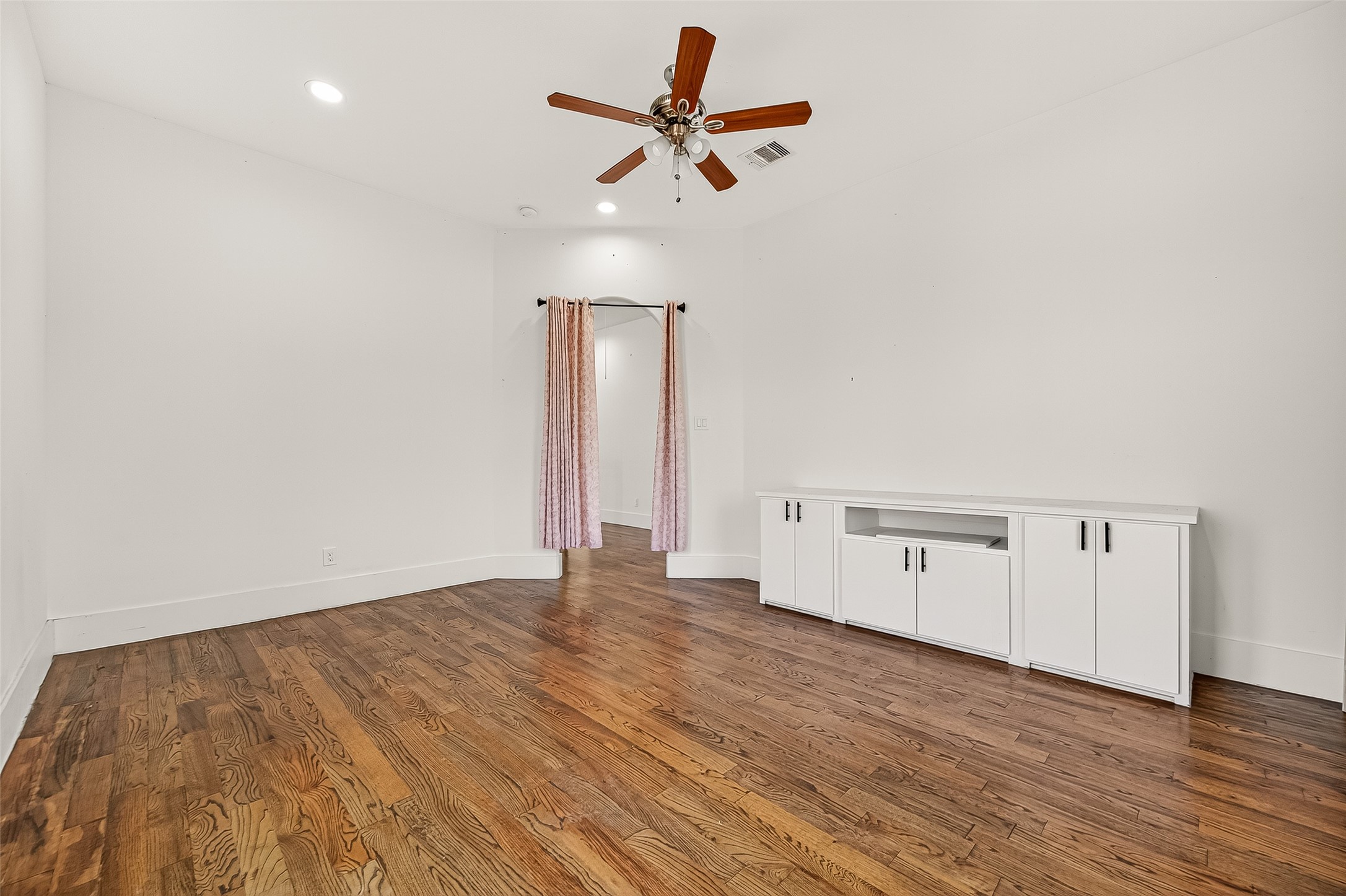 7915 Kirk Road Rosenberg, TX 77471 - Photo 21 of 28 This room features hardwood flooring, a ceiling fan, and neutral walls. It includes an en-suite bathroom and opens to a hallway with railing, offering a spacious and inviting atmosphere.
