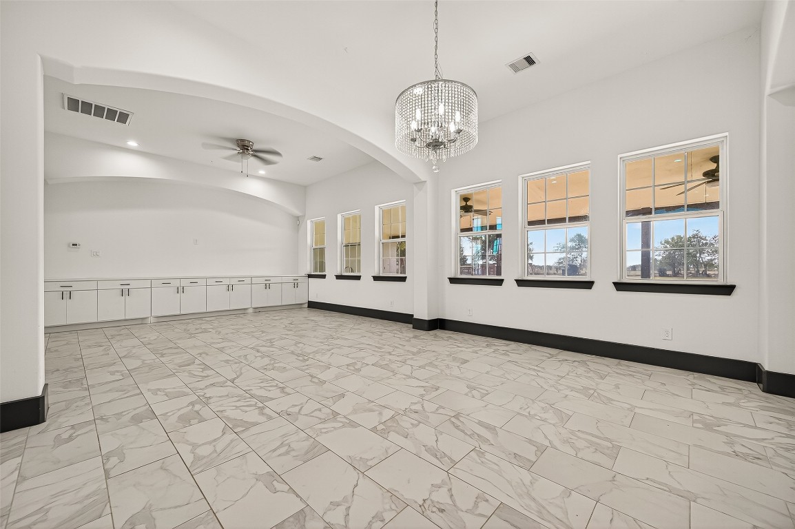 7915 Kirk Road Rosenberg, TX 77471 - Photo 4 of 28 This spacious room features elegant tile flooring, a modern chandelier, and ample natural light from multiple windows. The room is enhanced by a sleek ceiling fan and a long row of built-in cabinetry, perfect for storage. Ideal for gatherings or a versatile living space.