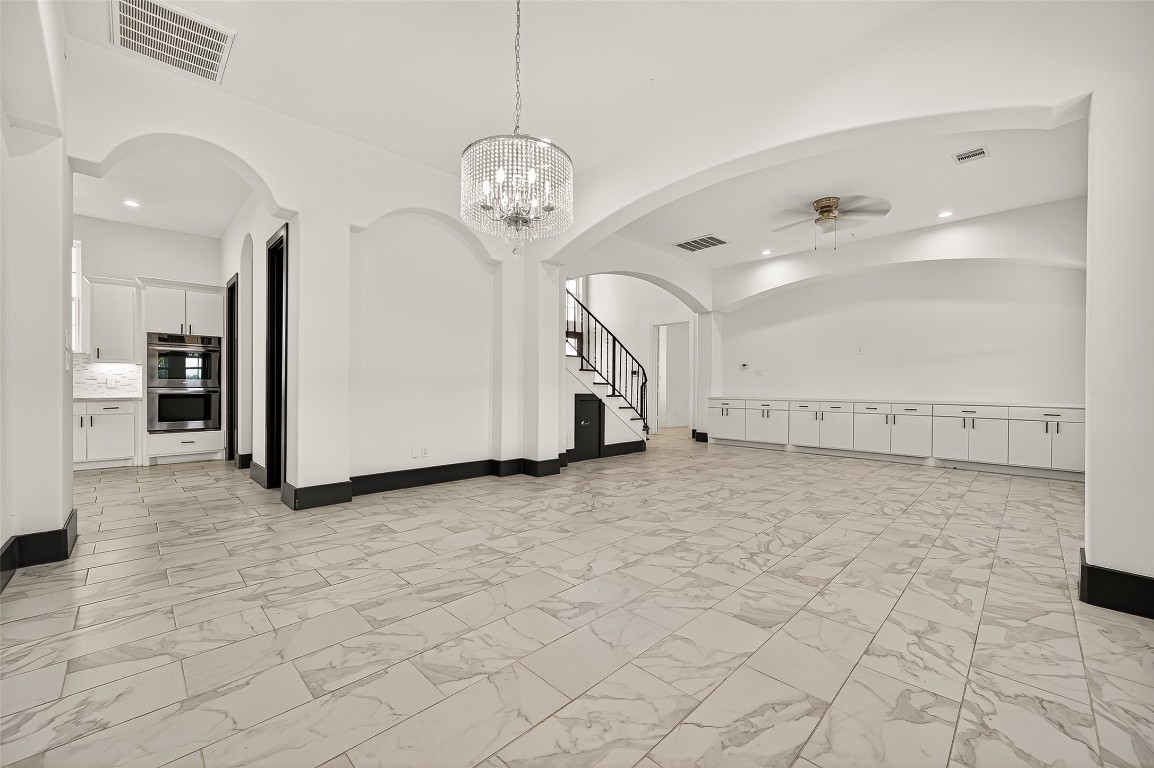 7915 Kirk Road Rosenberg, TX 77471 - Photo 5 of 28 This spacious, elegant room features marble-like tile flooring, a modern chandelier, and arched doorways. It includes ample built-in storage, a ceiling fan, and leads to a staircase with wrought iron railings. The open layout provides a bright, airy atmosphere.