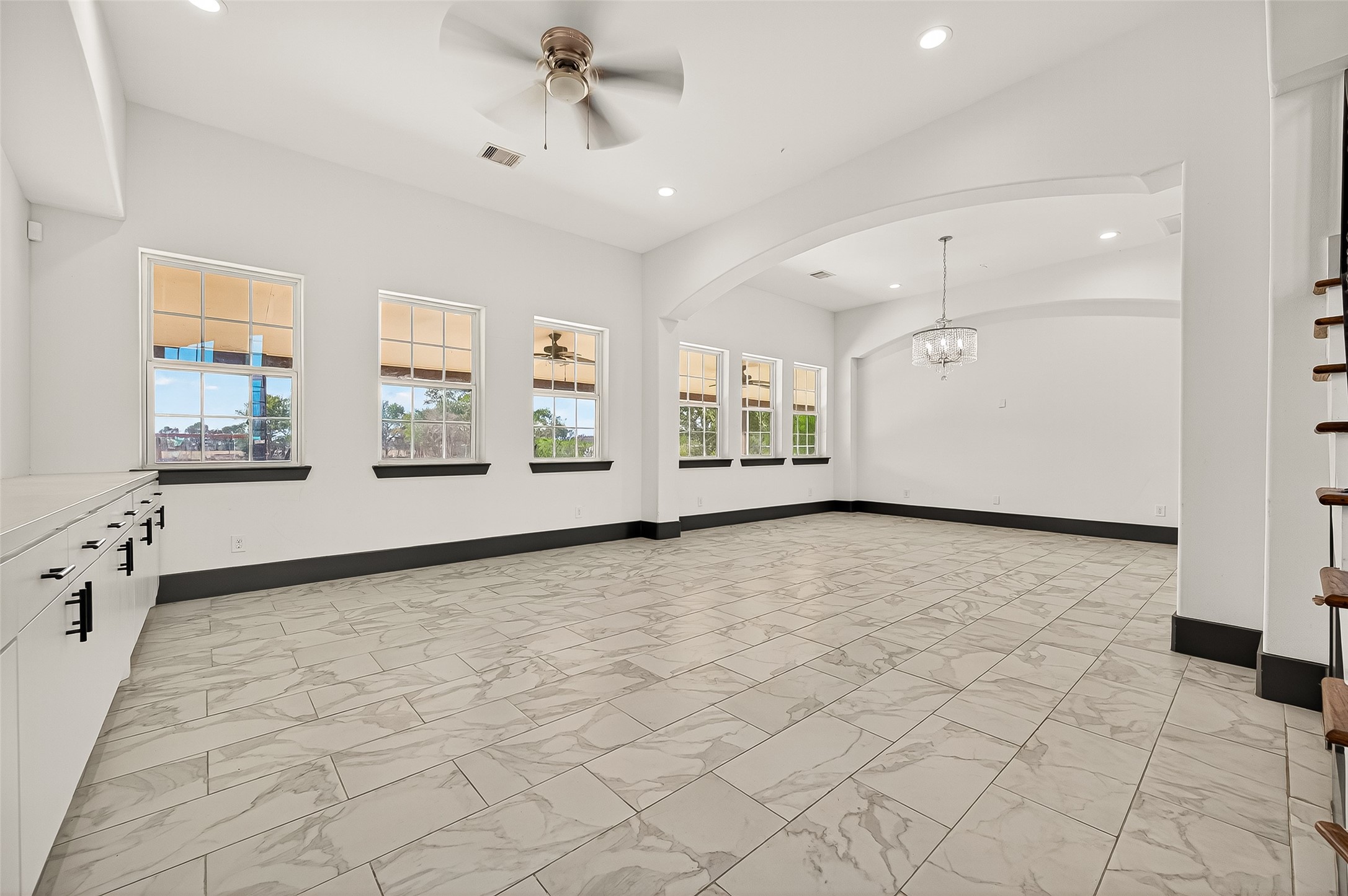 7915 Kirk Road Rosenberg, TX 77471 - Photo 7 of 28 This spacious, bright room features elegant tile flooring, large windows offering natural light, and a modern ceiling fan. The open layout includes a dining area with a stylish chandelier, perfect for entertaining.